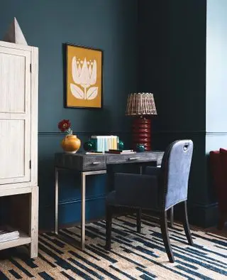 bureau à domicile avec murs ombrés, œuvres d'art jaunes, bureau, chaise rembourrée bleue, tapis bleu et crème, lampe rouge, unité de rangement