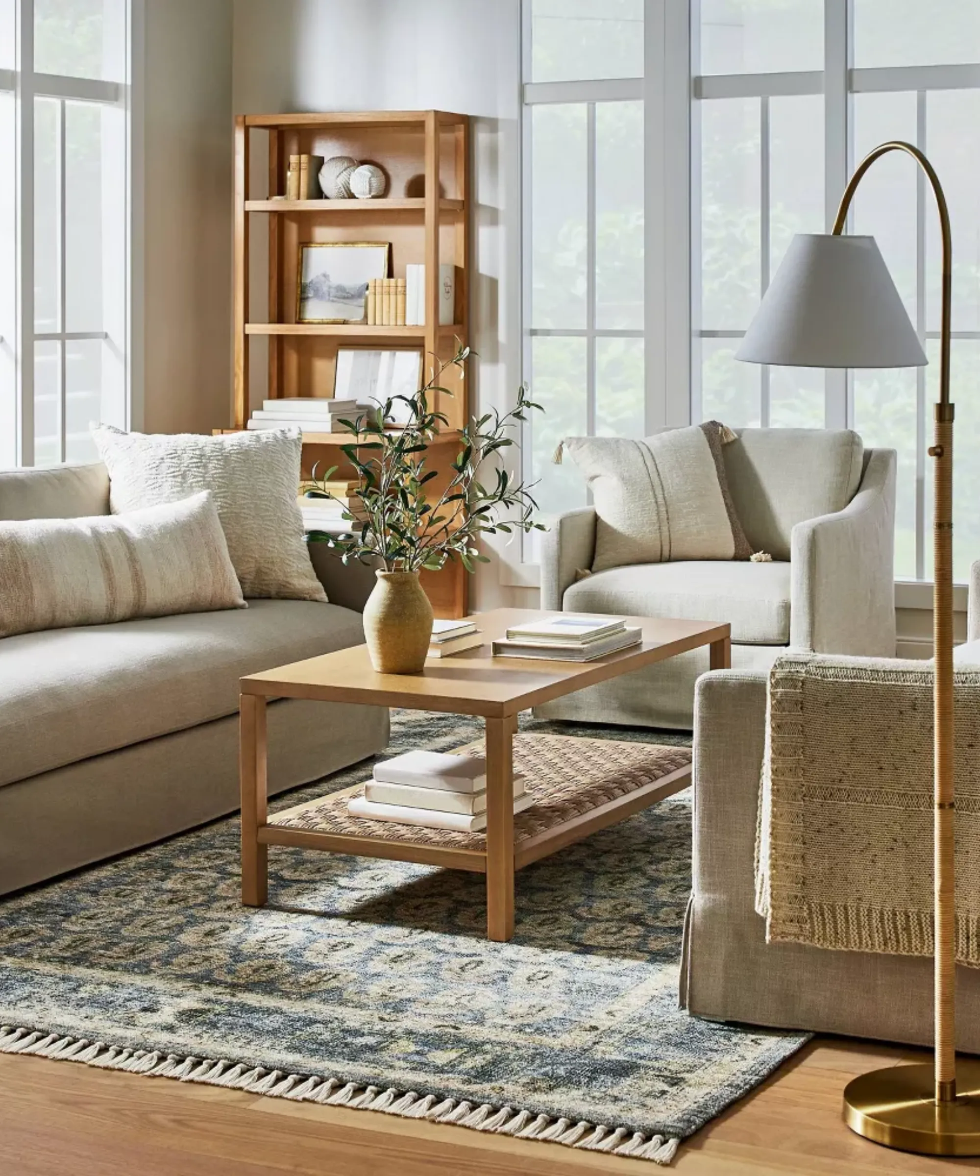 una sala de estar con un sofá beige, una silla decorativa beige, una mesa de centro rectangular de madera con un florero encima y una alfombra azul de inspiración persa en el suelo' loading='lazy' title=