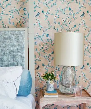 침대 옆 테이블과 어울리는 침대 뒤의 매우 섬세한 파스텔 꽃무늬 벽지를 보여주는 핑크 침실 아이디어