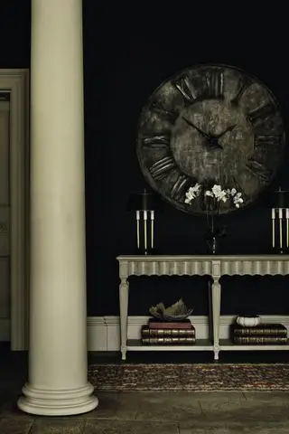 entrée noire avec sol en pierre, pilier en pierre, console et grande horloge