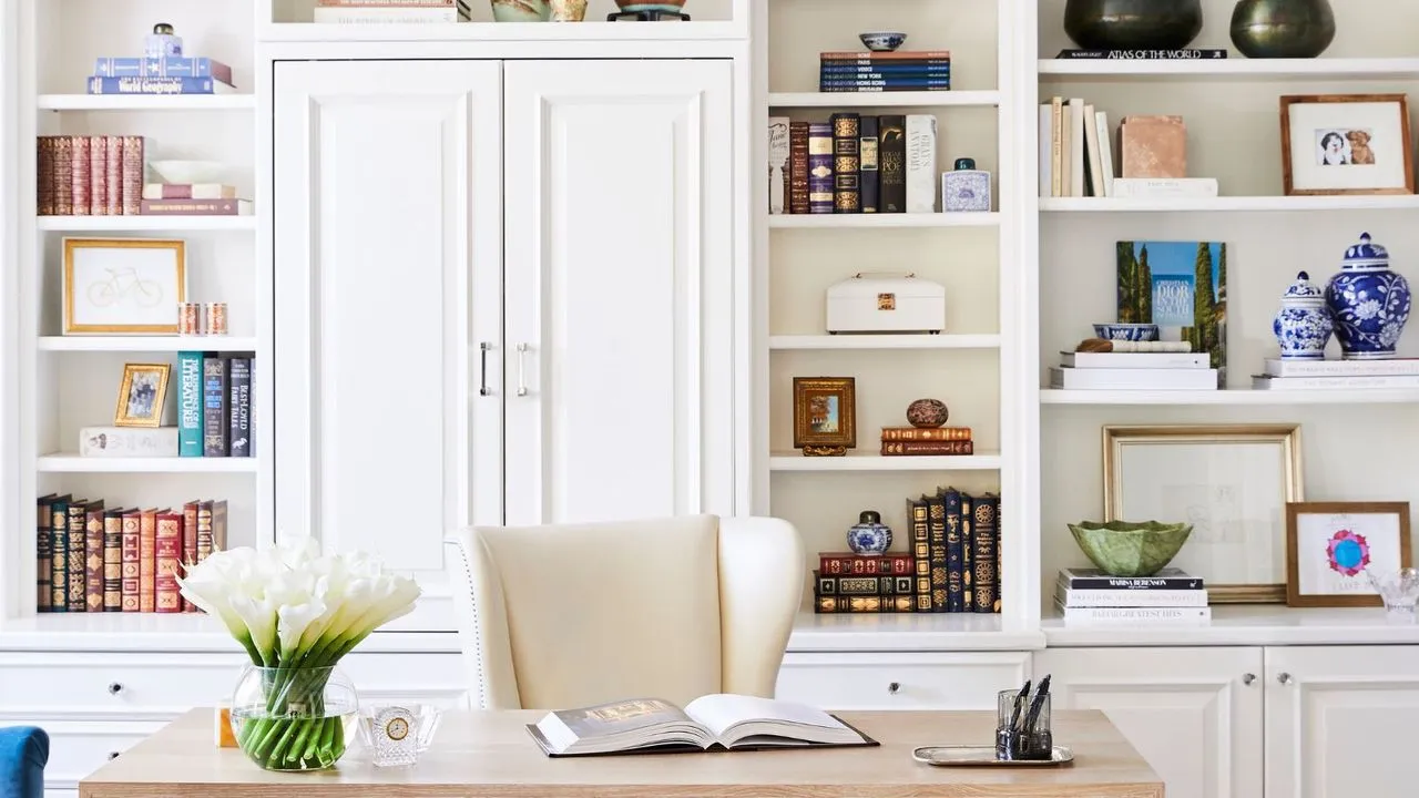 Całkowicie domowe biuro z wbudowanymi półkami i drewnianym biurkiem, książkami i bibelotami zdobiącymi półki' loading='lazy' title=
