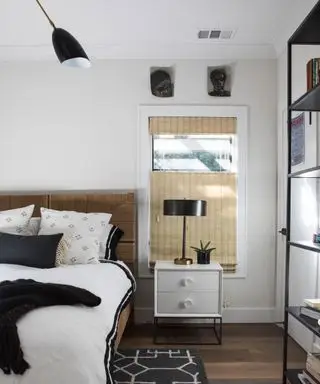 Chambre contemporaine avec murs peints en blanc et crème, parquet en bois foncé avec tapis noir, étagère, lit avec draps blancs, coussins dispersés