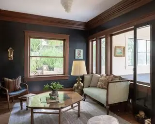 Salon traditionnel avec des détails en bois sombre sur les boiseries, un parquet en bois foncé, un tapis gris, une table basse en bois foncé, un petit canapé et une chaise avec un cadre en bois foncé, des fenêtres intérieures donnant sur le couloir