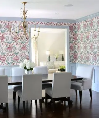 Salle à manger colorée avec papier peint à fleurs, boiseries et boiseries peintes en bleu ciel, suspension en forme d'ananas doré, parquet en bois foncé et table à manger rectangulaire, chaises de salle à manger rembourrées grises