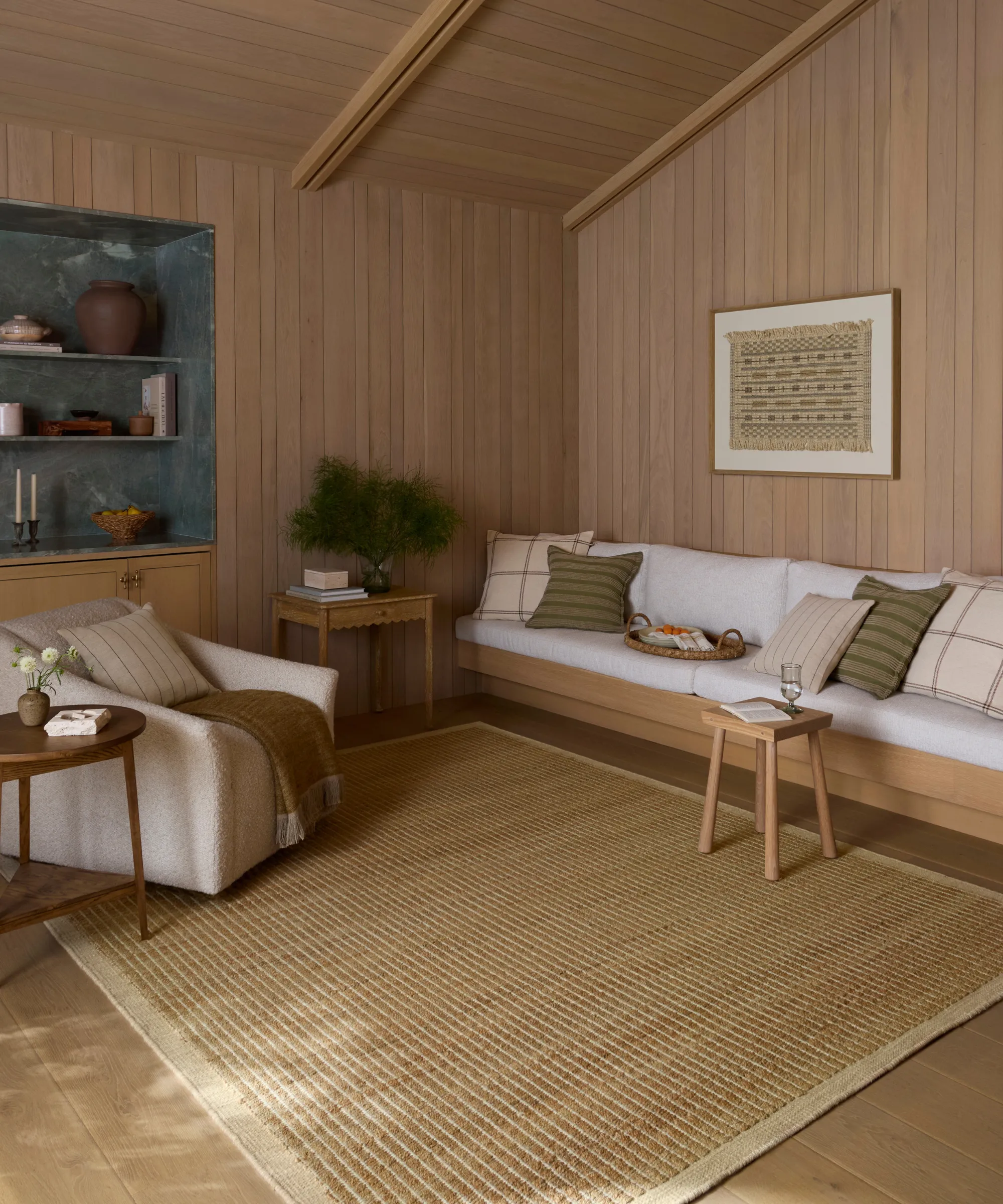 木製パネルの壁と天井のある暖かいリビングルームは、白いクッション付きの組み込みのソファとアクセントチェアとジュートラグ' loading='lazy' title=
