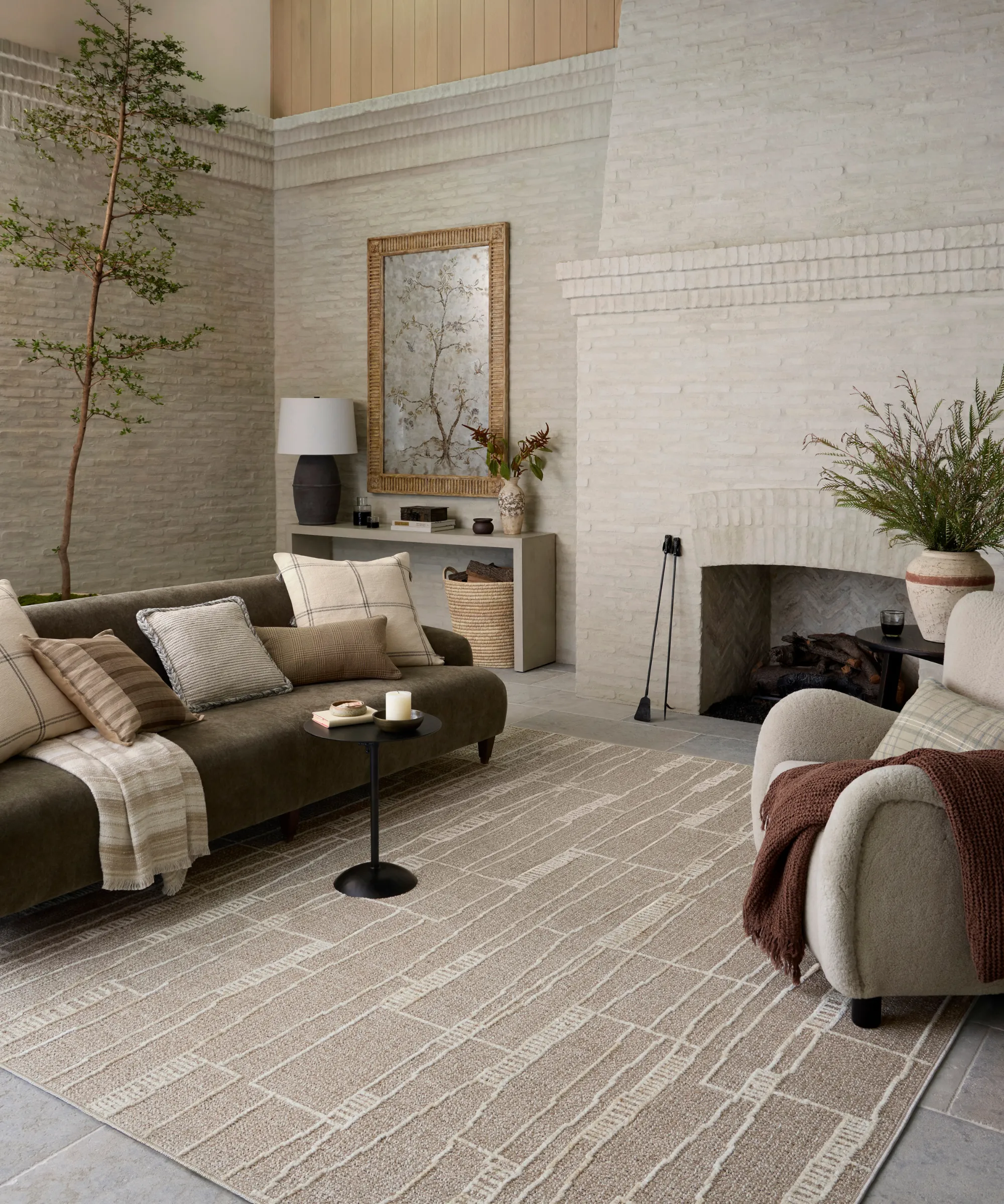 レンガの壁と大きなレンガの炉床のあるリビングルームは、様々な枕のある濃い緑色のソファの小さな黒い飲み物テーブル日焼けにハイロー山の敷物と右側のアクセントチェア' loading='lazy' title=