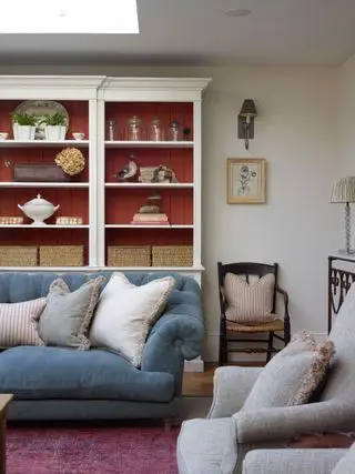 salon avec canapé bleu et fauteuil gris avec étagères blanches lambrissées rouges