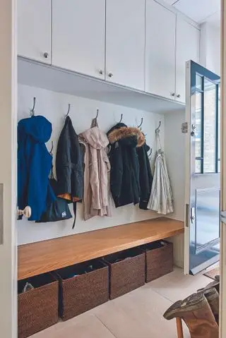 Entrada com piso de pedra, casacos em cabides com banco e cestos abaixo e armários acima