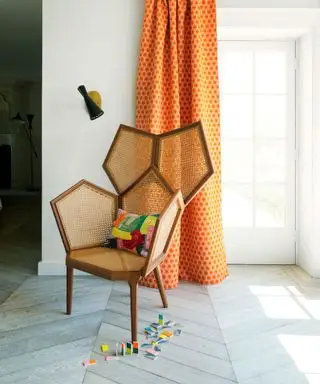 Un salon moderne du milieu du siècle avec une chaise en rotin, un drapé orange et des murs blancs.