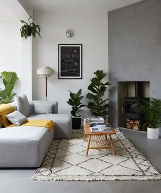Un salon moderne du milieu du siècle avec des murs et un sol gris, une table basse en bois et un canapé gris avec un jeté jaune.