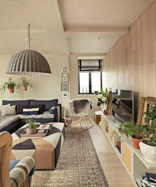 Vista a lo largo de la sala de estar, piso de madera con una alfombra grande y mesa de café central, mueble multimedia bajo con televisor y accesorios.