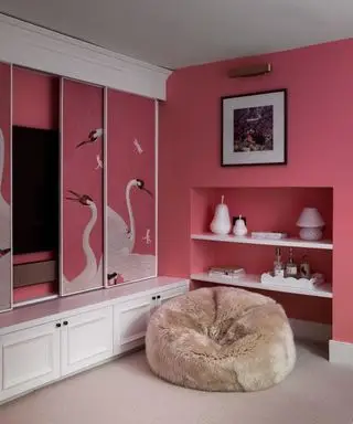 Salón pintado de rosa oscuro, con mampara corredera a medida con mural, puf marrón y estantería integrada en la pared con accesorios decorativos