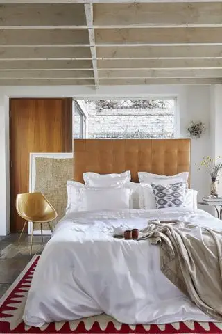 chambre avec poutres apparentes, sol en pierre, tête de lit en cuir, chaise design moderne, literie en soie blanche, murs blancs