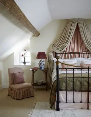 chambre mansardée avec baldaquin, lit en fer, tapis en coco, chaise rembourrée, table d'appoint, tapis, poutre, roses