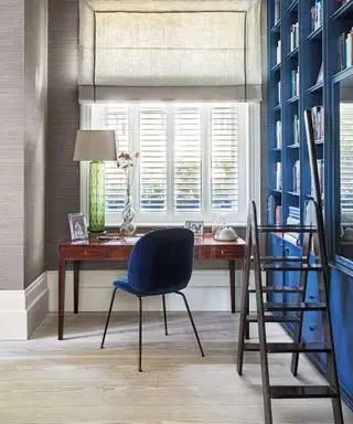 Bureau avec bureau à côté de la fenêtre, placards intégrés et bibliothèques bleu foncé.