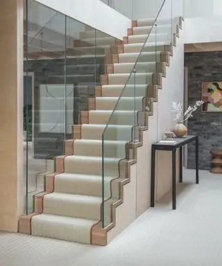 Cremefarbener Teppich auf Holztreppe, Flur mit passendem Teppich, schwarzer Konsolentisch.