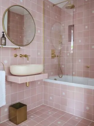 salle de bain rose avec carrelage carré rose, luminaires et accessoires dorés, lavabo flottant