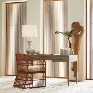 oficina en casa con listones en las ventanas, escultura de madera, escritorio de madera, alfombra de piel de oveja mullida, lámpara, silla de ratán