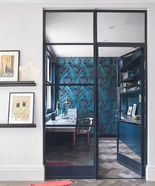Un petit bureau avec des portes vitrées peintes en bleu foncé avec un mur décoratif et du parquet.