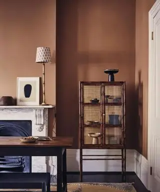 Spisestue med svart tregulv, brune vegger, hvit koving og gulvlister og mørke tremøbler på et grått, gult og hvitt teppe