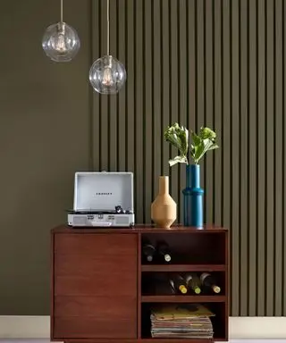 Une commode avec un tourne-disque et un vase devant un mur vert olive