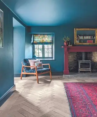 Salon avec murs peints en bleu et cheminée, chaise longue à côté d'un tapis rose