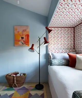 Chambre d'enfant peinte en bleu pâle avec du papier peint à motifs rouges autour d'un lit en alcôve