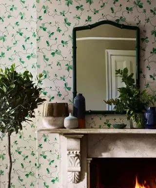 Papel pintado floral verde, chimenea con espejo verde colocado encima, plantas de interior, adornos en la repisa