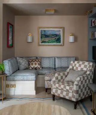 Pequeño salón moderno con sofá incorporado, sillón a cuadros, pintura y apliques en la pared, alfombra festoneada con suelo de madera