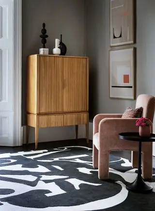 Salon gris avec un tapis noir et blanc et une chaise rose poudré