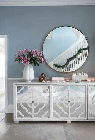 En skjenk med speil og speil over i en gang med lyseblå vegger med en refleksjon av rekkverk med en krans