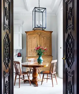 En regardant à travers les portes en acajou d'époque ouvragées dans la cuisine avec table ronde et chaises de style campagnard et commode en noyer