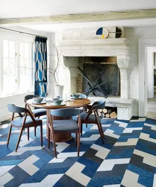 Salle à manger traditionnelle avec murs en bois lambrissés blancs, plafond peint en blanc, grande cheminée en pierre, moquette en carrelage à motifs géométriques, coloris bleu, blanc et crème, rideaux assortis, bois sombre, table à manger arrondie, quatre chaises de salle à manger dans le noir bois avec revêtement d'assise et de dossier bleu