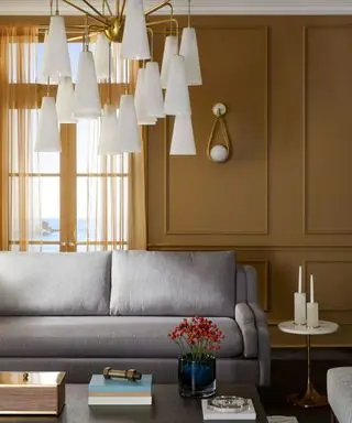 Salon jaune avec canapé gris, grand lustre bas, appliques murales assorties, table basse