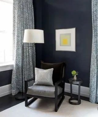 Coin de salon, murs peints en bleu, fauteuil gris foncé et noir, rideaux à motifs bleus