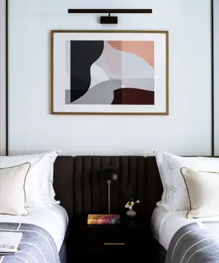 Et sæt to enkeltsenge med et bord imellem og et maleri indrammet på væggen.