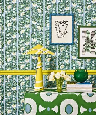 Papier peint à fleurs bleu et blanc, bordure jaune, lampe de table jaune, buffet à fleurs vert et blanc décoré de livres et d'ornements