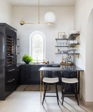 בר ביתי עם ארונות שחורים ומשטח עבודה עם חומרי זהב ומדפים
