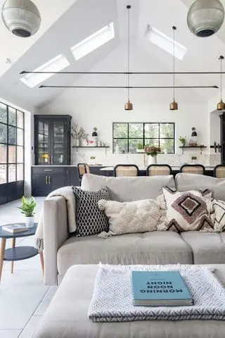 canapé blanc dans une cuisine ouverte avec fenêtres à ossature d'acier et plafond voûté et armoires de cuisine grises derrière