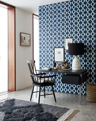 Geometrisch blau-weiß bedruckte Tapete in einem Heimbüro mit schwarzem Tisch und Stuhl.