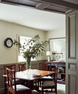 Salle à manger traditionnelle avec murs et lambris peints en vert, table à manger sombre avec quatre chaises assorties, plante au centre de la table, armoire en bois avec lampe de table et candélabre et carte encadrée