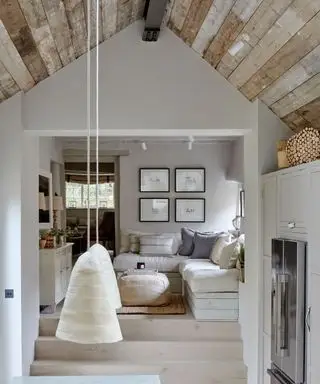 Vue depuis la cuisine ouverte sur le séjour. Ancien bureau de poste restauré. Plafond rustique lambrissé, pendentifs bas, murs peints en gris et armoires de cuisine