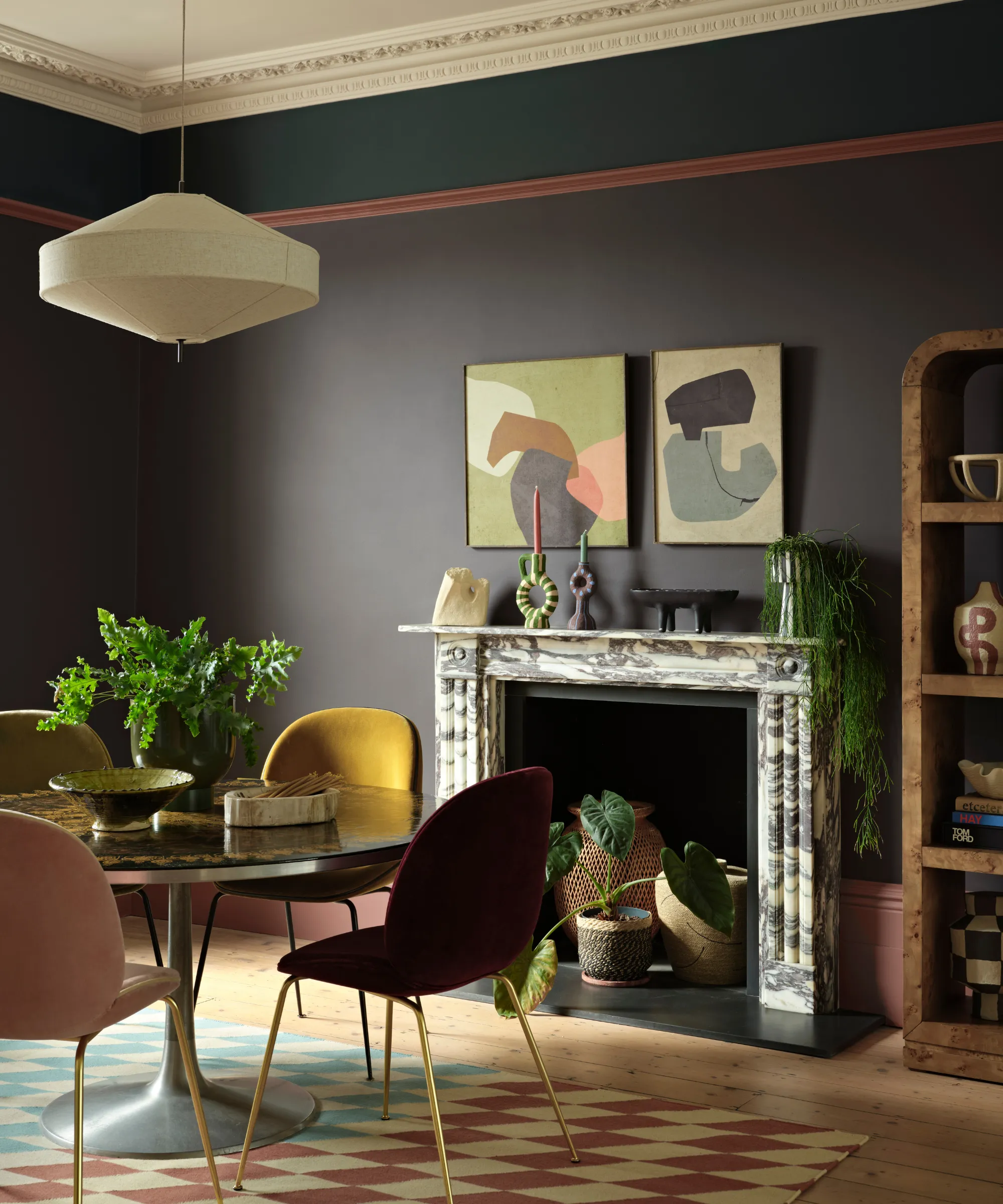 en spisestue med et lite rundt spisebord med fire fargerike stoler en peis laget av marmor med dekorative gjenstander på mantelen en pendel av stoff hengende over bordet og vegger malt med Benjamin Moores Silhouette' loading='lazy' title=