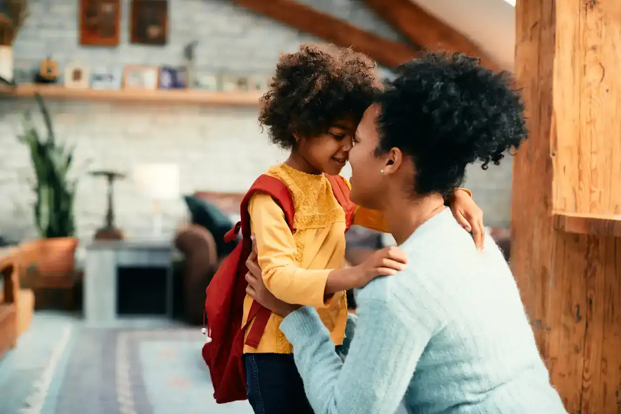 Affectionate African mother talking to her small daughter while saying goodbye before going to school for the first time.