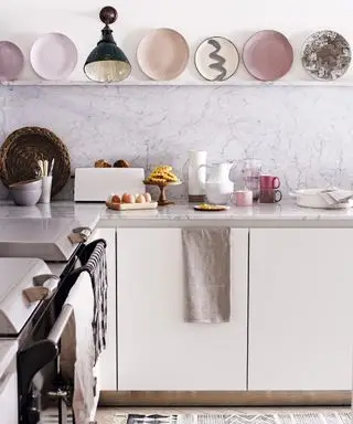 Idées de couleurs de cuisine roses dans un décor blanc avec une sélection d'assiettes rose pâle exposées sur des étagères ouvertes.