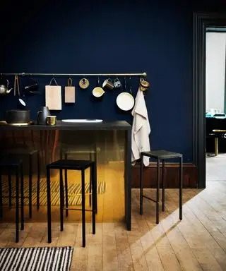 Idées de couleurs de cuisine en bleu foncé avec parquet et îlot en laiton avec tabourets noirs.