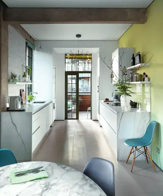Une cuisine blanche moderne avec un mur vert citron, des chaises bleu sarcelle et des surfaces en marbre.