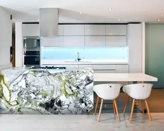 Spazio cucina moderno con isola cucina in marmo bianco, posti a sedere al piano inferiore dell'isola, mobili da cucina bianchi, pavimento grigio