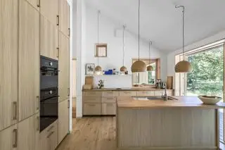 Sol de cuisine en bois massif dans un décor naturel avec armoires en bois, murs blancs et luminaires suspendus.