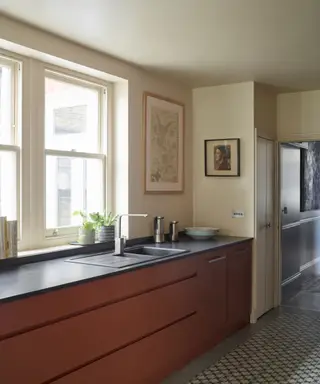 Et kjøkken med stort vindu og rødbrune skap